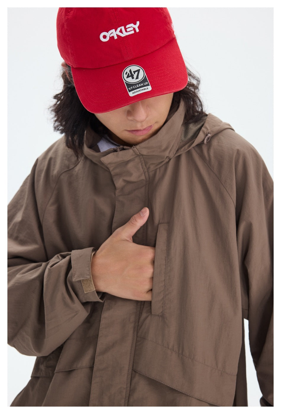 Close-up of a taupe jacket's covered front closure and chest pocket, with a model's hand tucked inside.