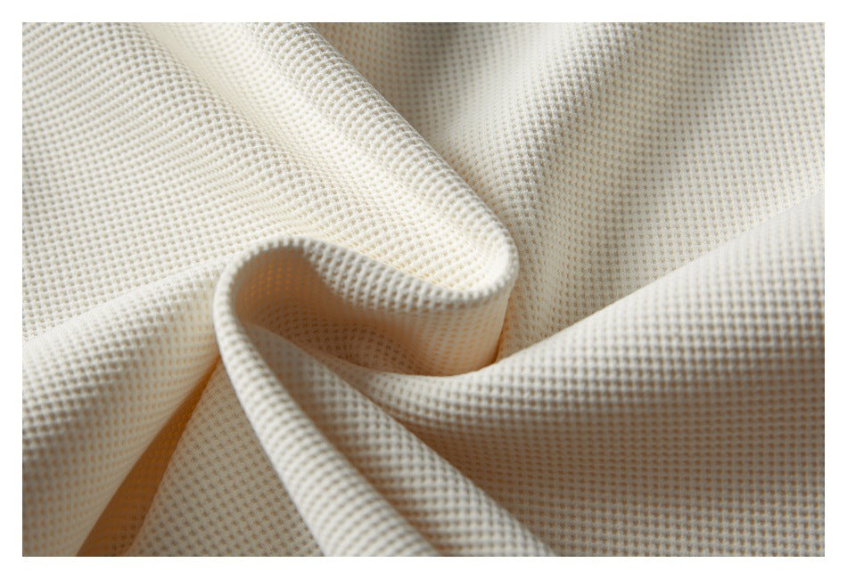 Macro view of the cream garment's textured waffle-knit fabric draped in soft folds.