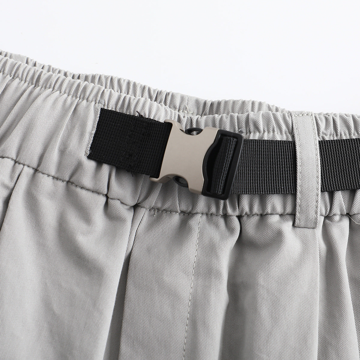 Close-up of the light gray shorts' gathered waistband and black adjustable belt with a metal-and-plastic buckle.