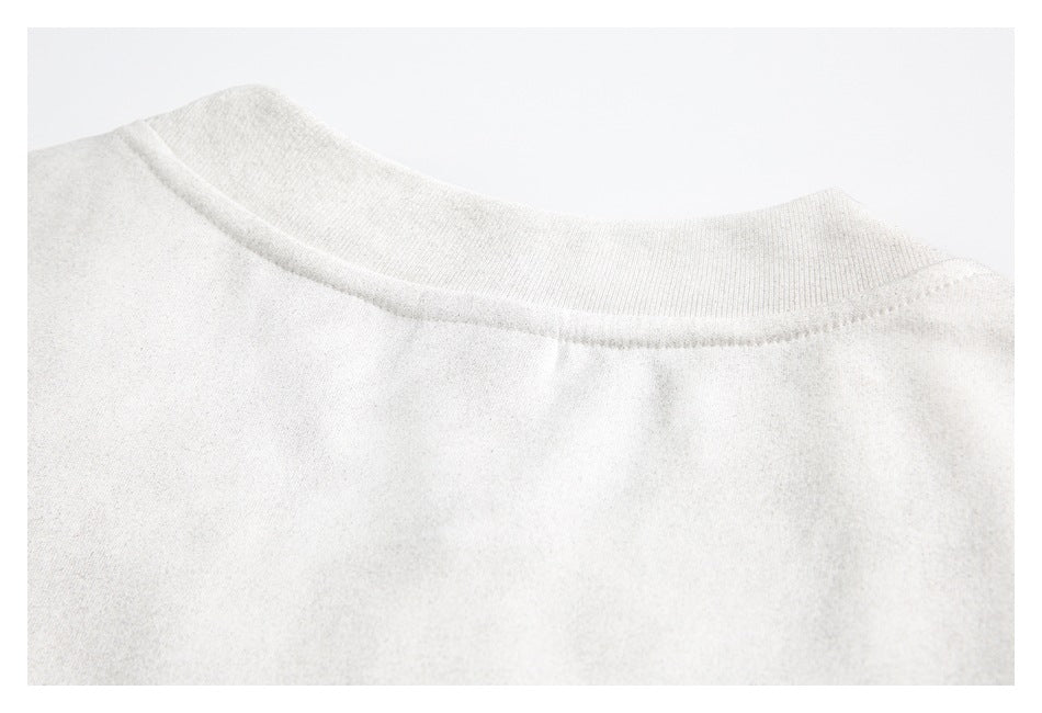 Close-up of the ribbed crew neckline and shoulder seam on an off-white top.