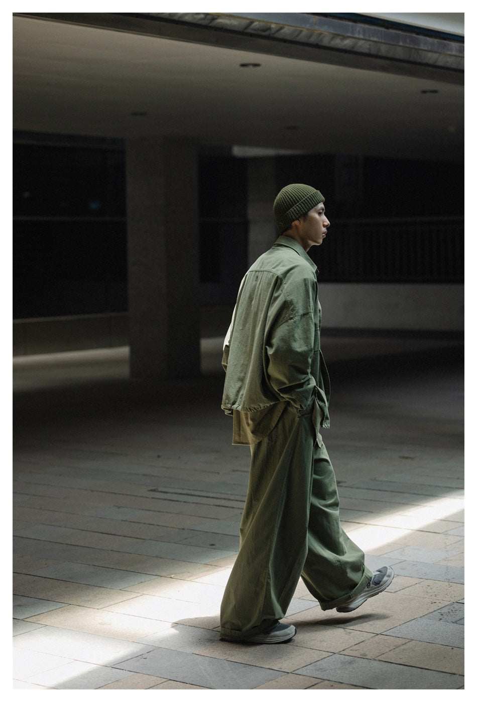 Side view of a model wearing a sage green oversized jacket and loose trousers with a matching ribbed beanie.