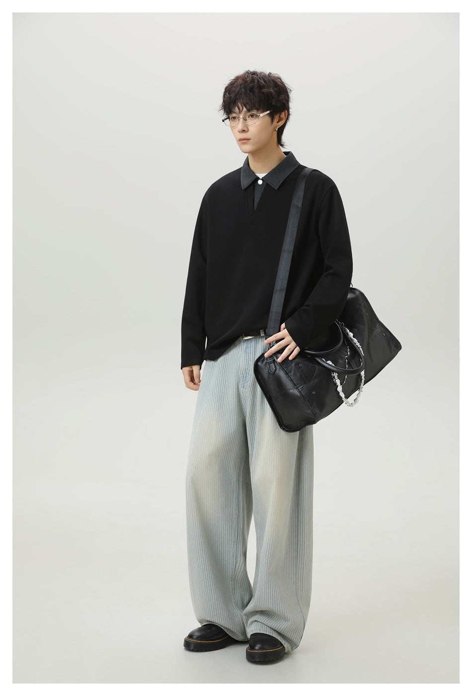 Model wearing a black long-sleeve collared pullover with pale wide-leg striped trousers and carrying a black shoulder bag.