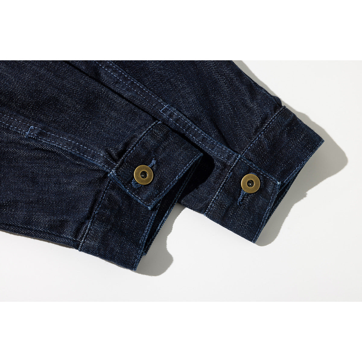 Close-up of a dark indigo denim jacket sleeve cuff with brass buttons and contrast stitching.