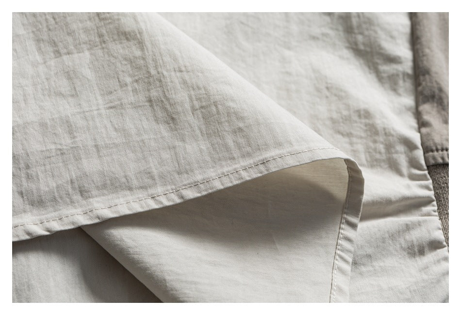Close-up of a light gray-beige garment hem, showing its folded edge and stitching.