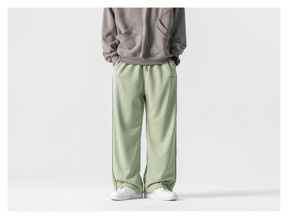 Model wearing loose pale sage-green wide-leg pants with a gray hoodie and white sneakers, front view.