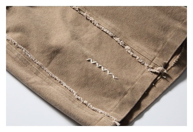 Close-up of tan trousers with frayed seam detailing and a small white zigzag stitch.