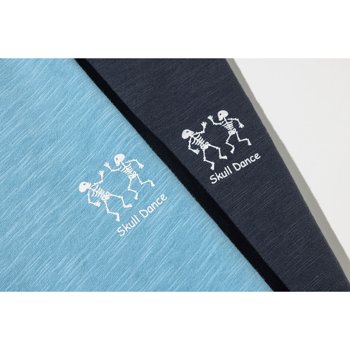 Close-up of light blue and dark navy T-shirts, each printed with two dancing skeletons and “Skull Dance.”
