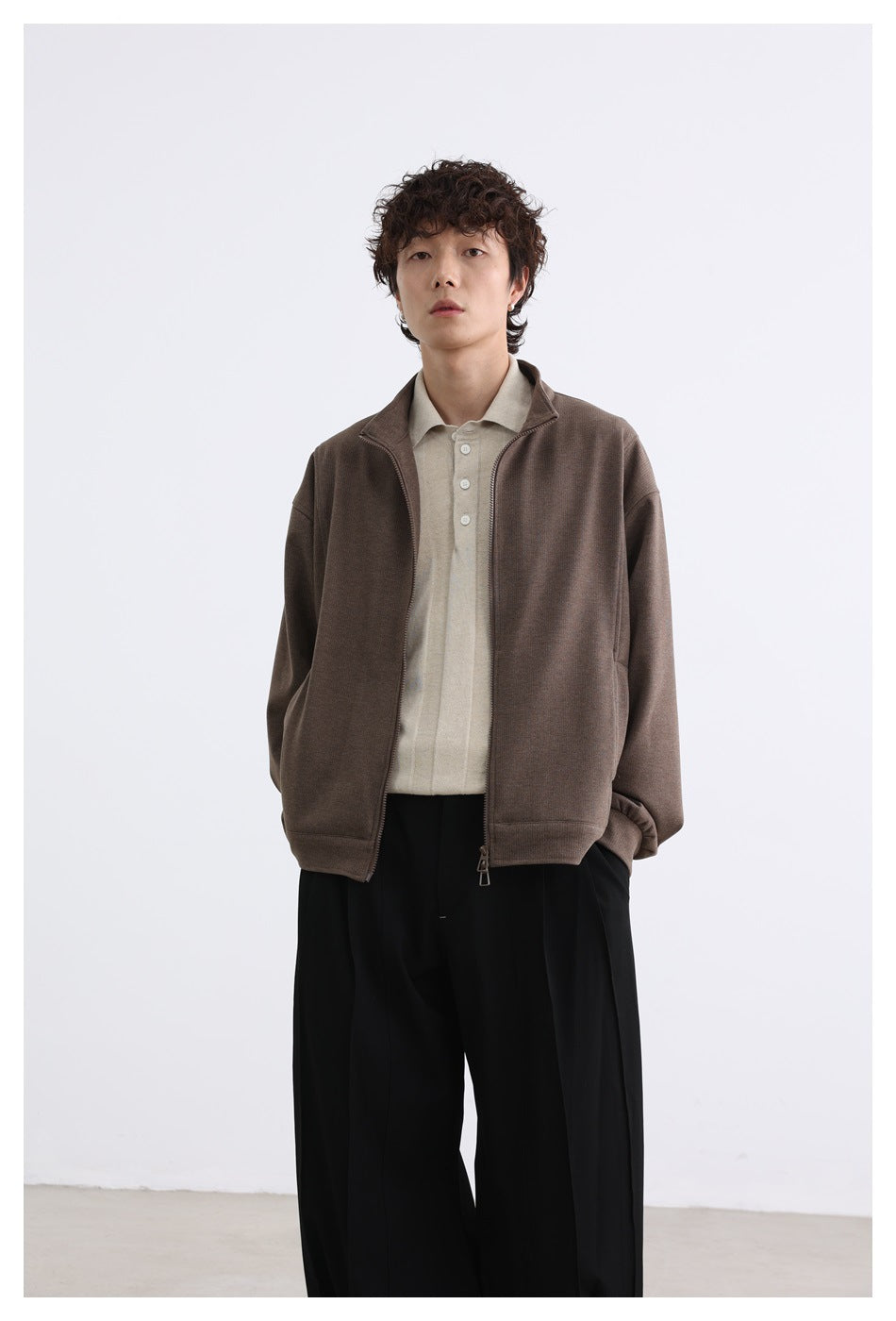 Model facing forward in an open brown zip-front jacket with a raised collar and roomy sleeves.