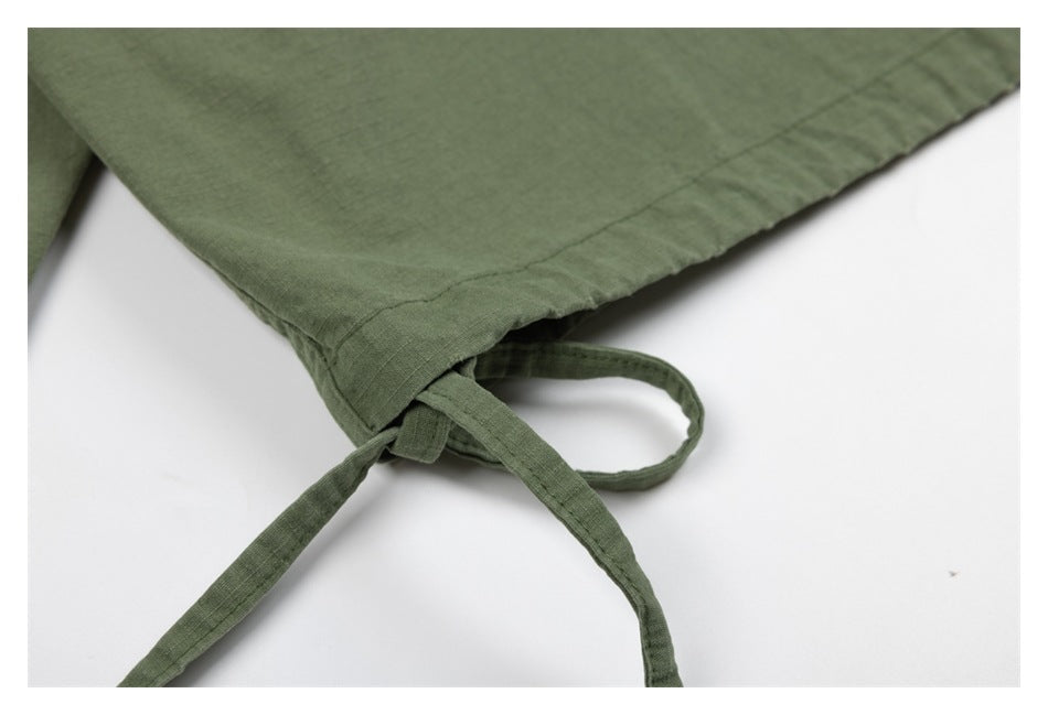 Close-up of olive-green garment fabric with stitched seams and attached ties on a white background.