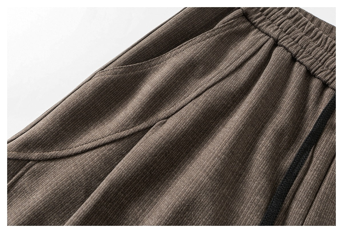 Close-up of taupe trousers showing a slanted pocket opening and gathered waistband.