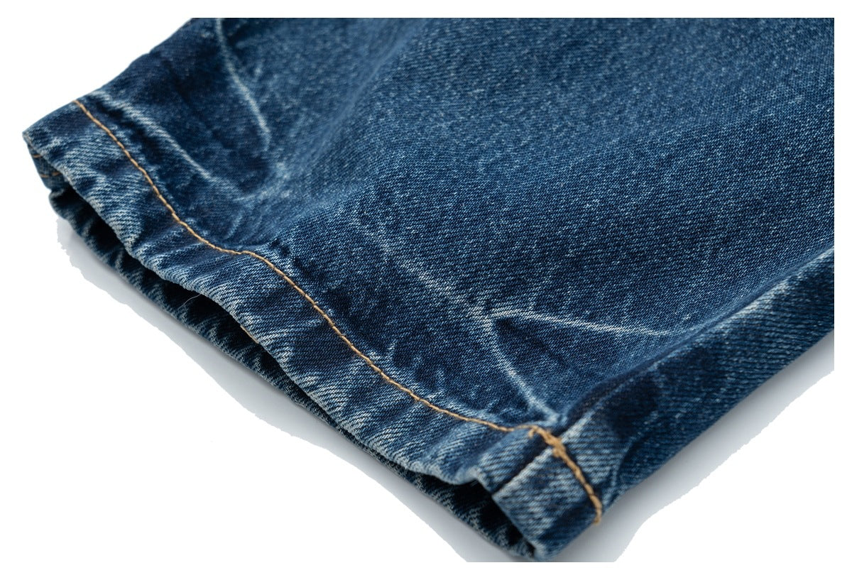 Close-up of a folded hem on dark blue denim with tan stitching.