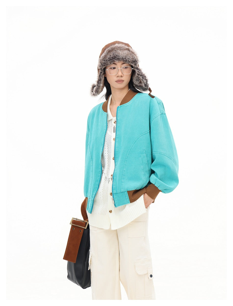 Closer view of a model wearing a turquoise bomber jacket with brown trim and a cream knit cardigan.