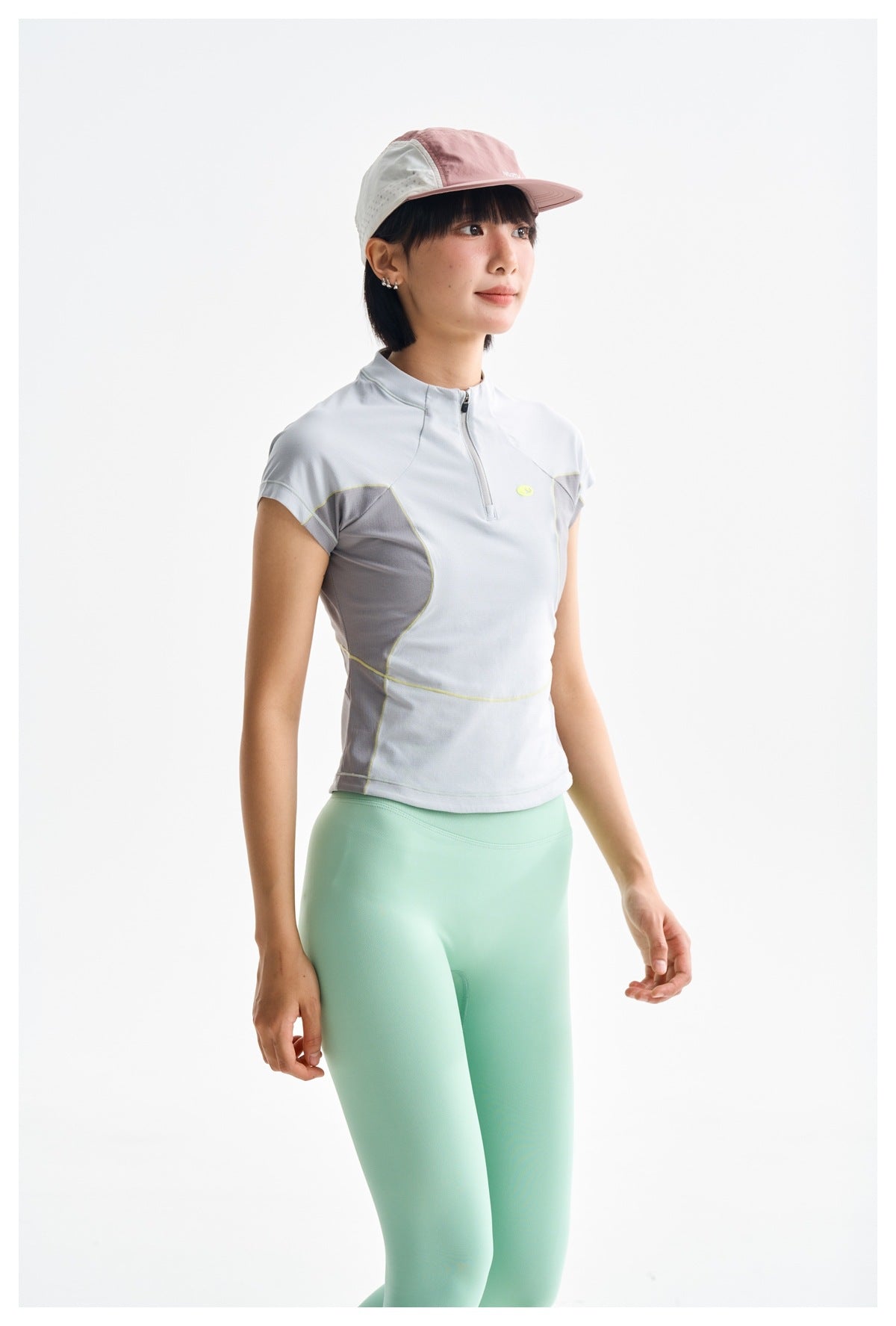 Three-quarter view of a model in a light gray quarter-zip top with lime piping and mint leggings.