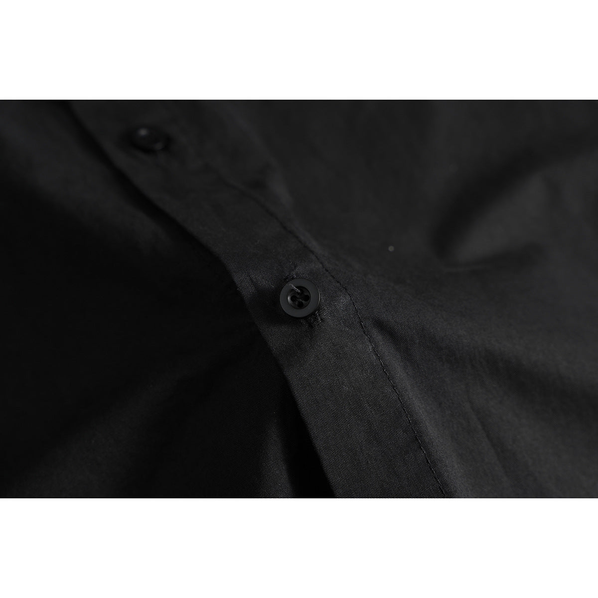 Close-up of a black shirt's front placket and dark button.