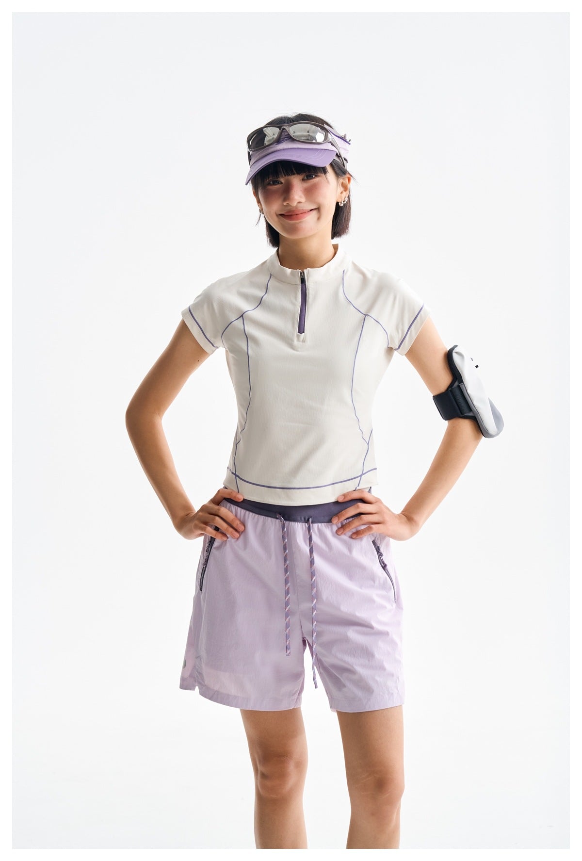 Model wearing a white short-sleeve zip-neck top with lavender piping and pale lavender shorts.