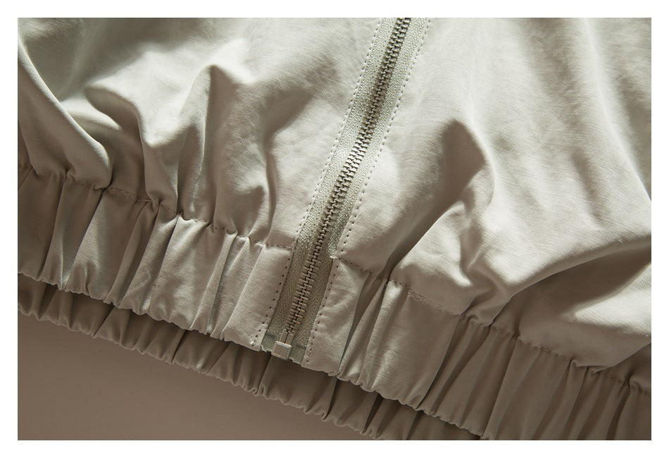 Close-up of a light beige jacket's gathered elastic hem and front zipper.