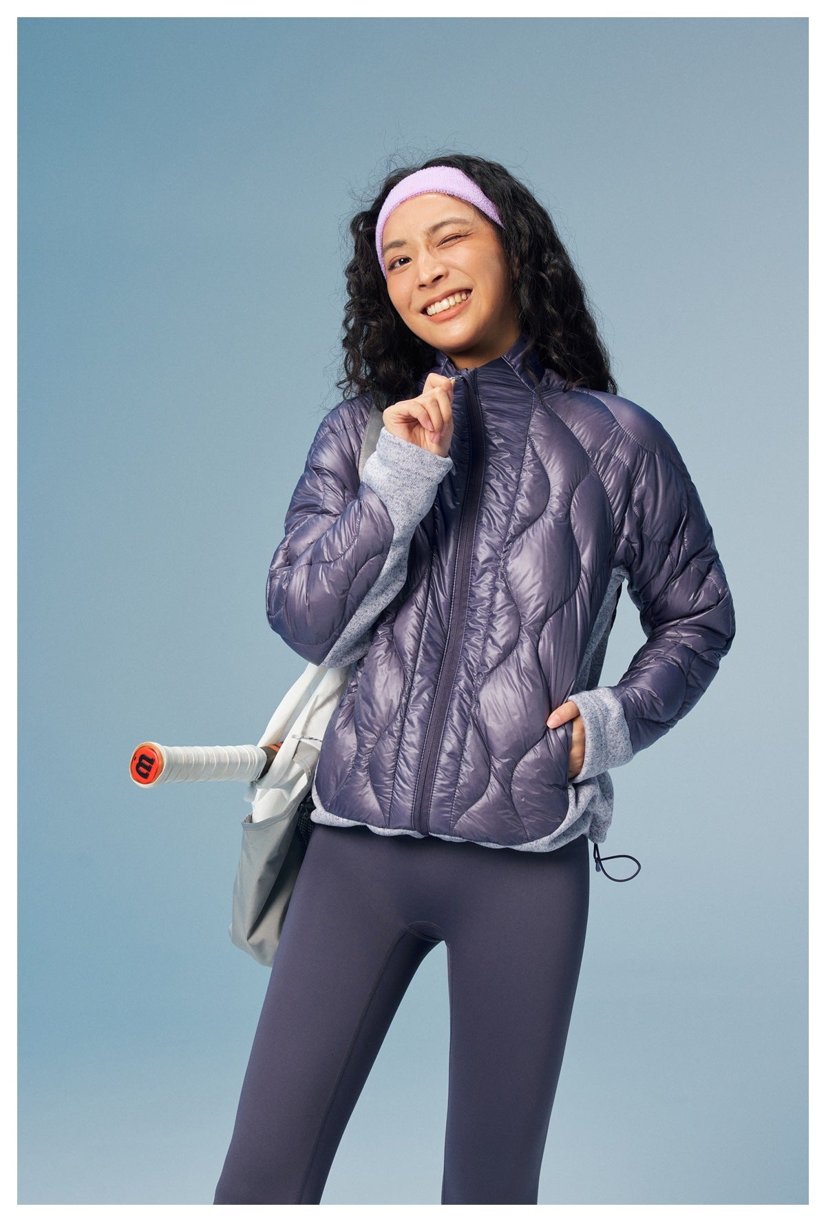 Model wearing a purple quilted zip jacket with gray panels, shown from the front with a shoulder bag.