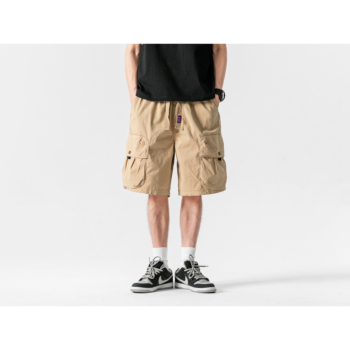 Front view of a model wearing tan cargo shorts with oversized flap pockets and a drawstring waist.