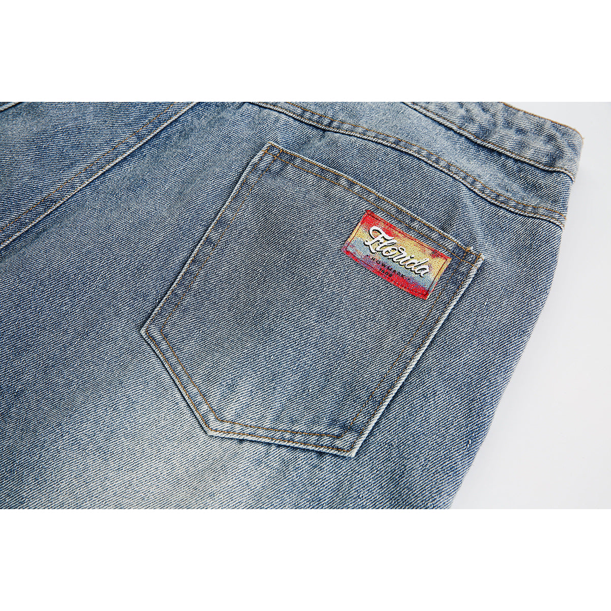 Close-up of a rear pocket with a small red-and-yellow label on faded blue denim shorts.