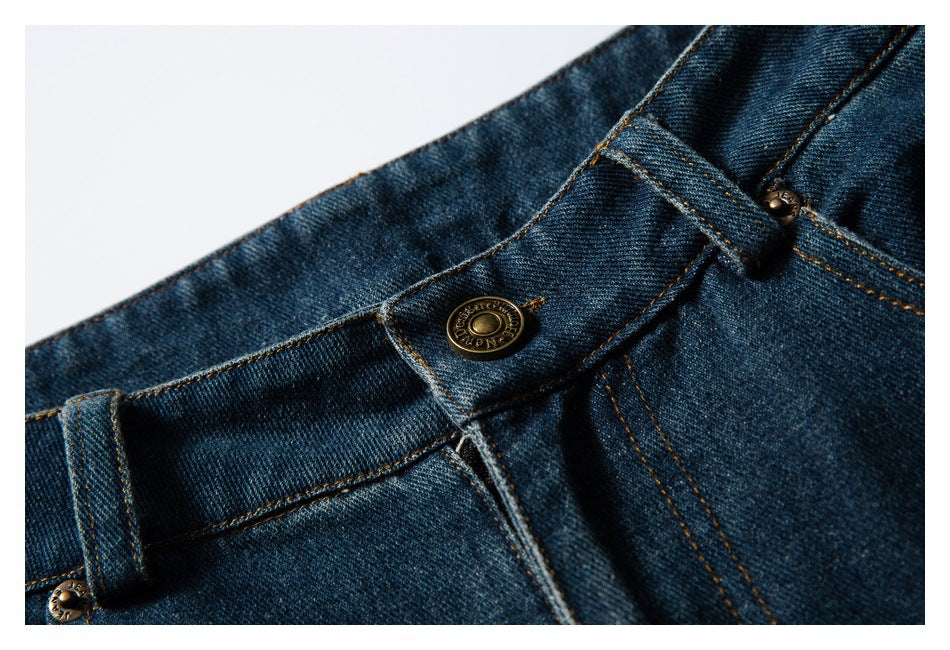 Close-up of the dark blue jeans waistband, metal button, belt loop and orange topstitching.