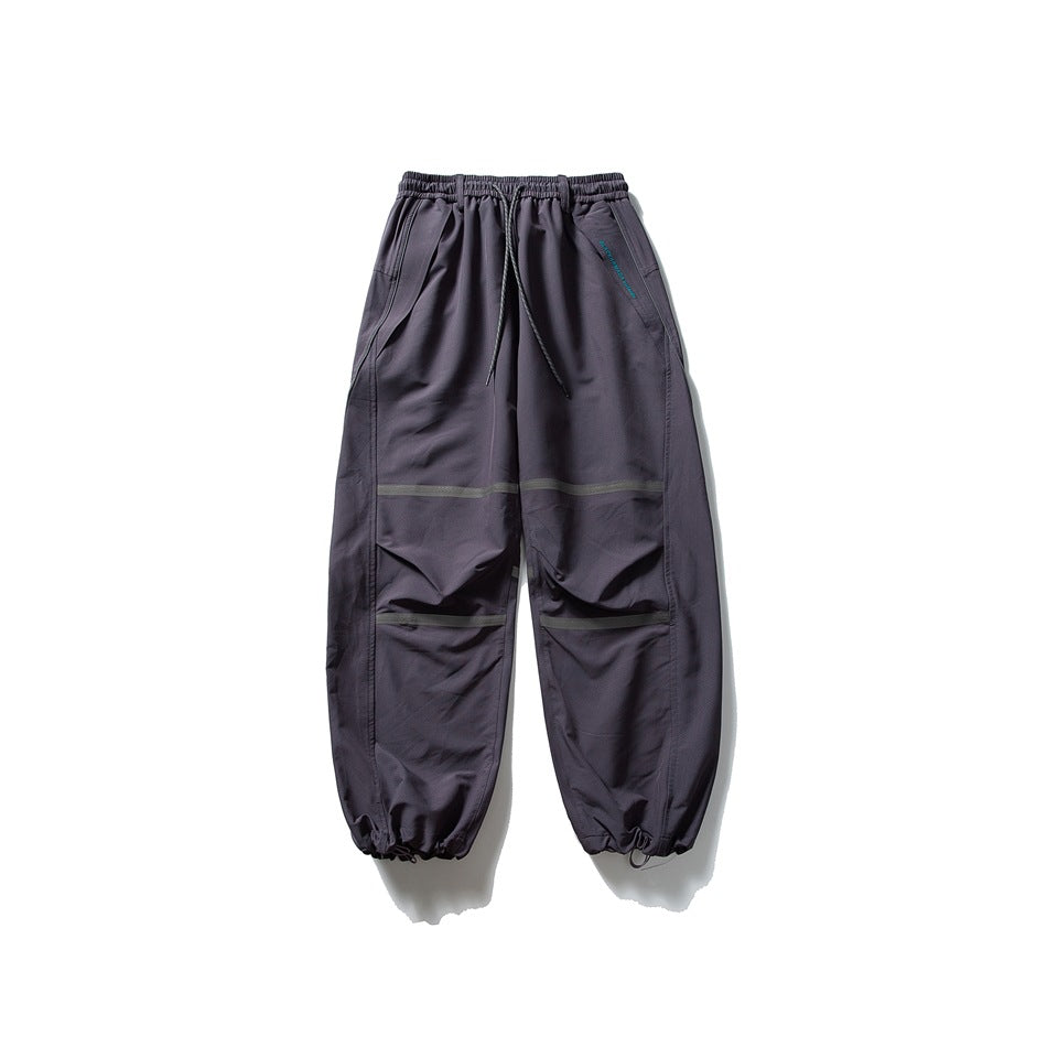 Dark purple-gray relaxed pants with drawstring waist, gray stripes and toggle ankle hems, laid flat