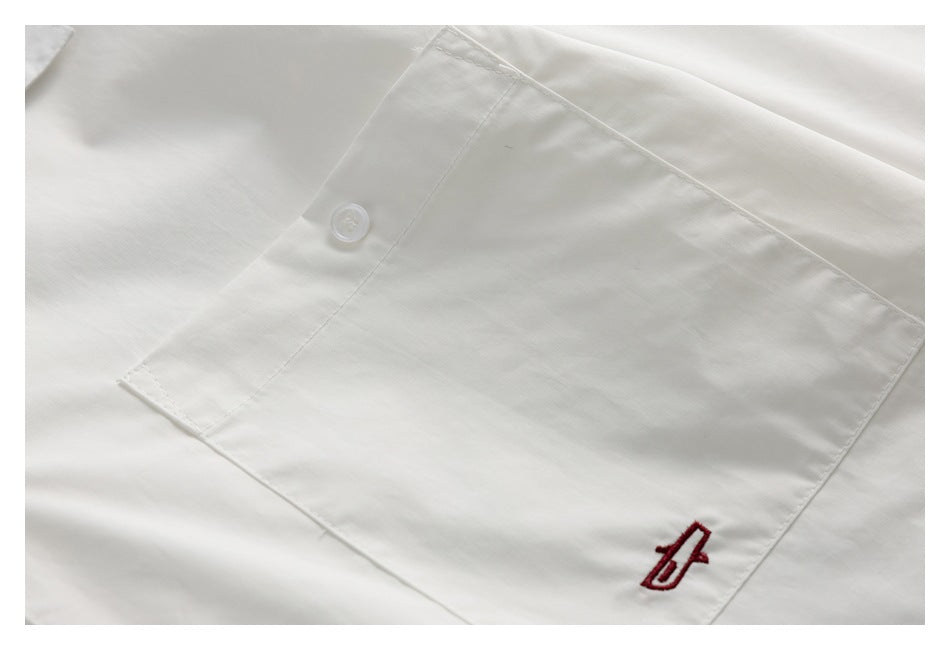 Close-up of a white shirt pocket with a white button and a small red embroidered emblem.