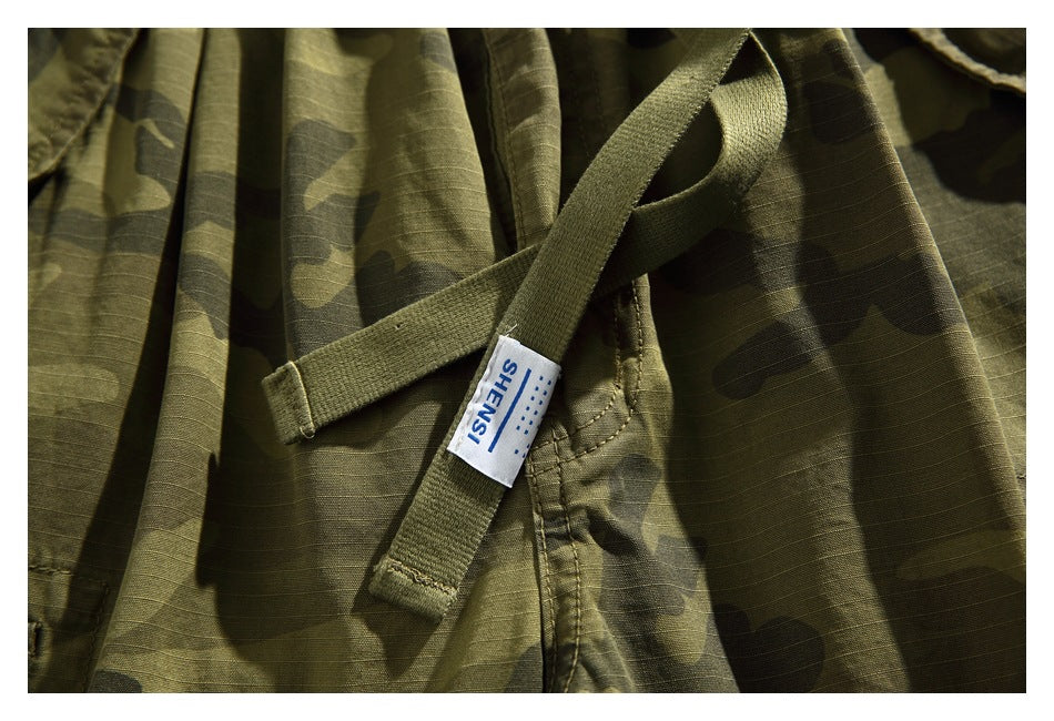 Close-up of olive camouflage shorts with stitched webbing and a white SHENSI label.