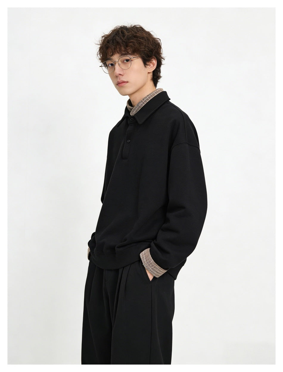 Angled view of a model wearing a black collared pullover with checked shirt collar and cuffs.