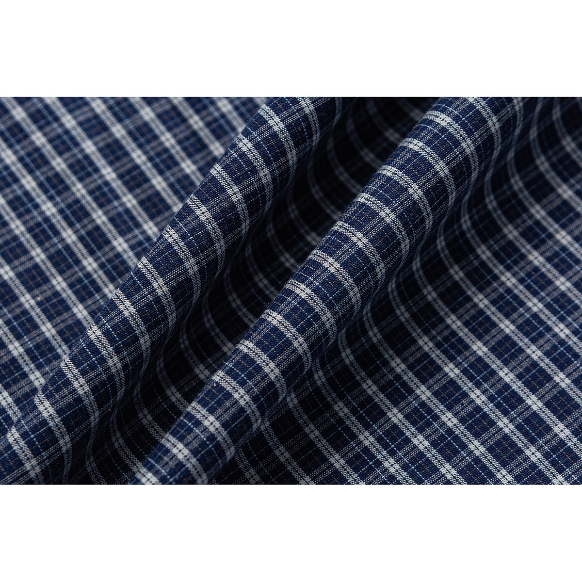 Close-up of navy plaid fabric arranged in folds, showing its intersecting light-colored lines.