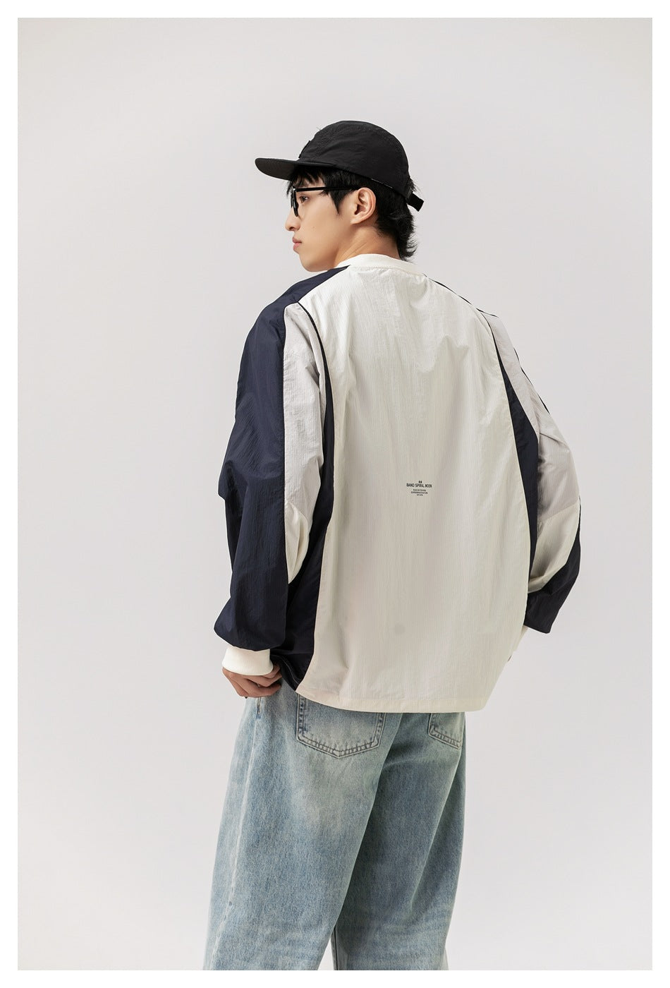 Angled rear view of a model wearing an oversized ivory pullover with navy panels and light-wash jeans.