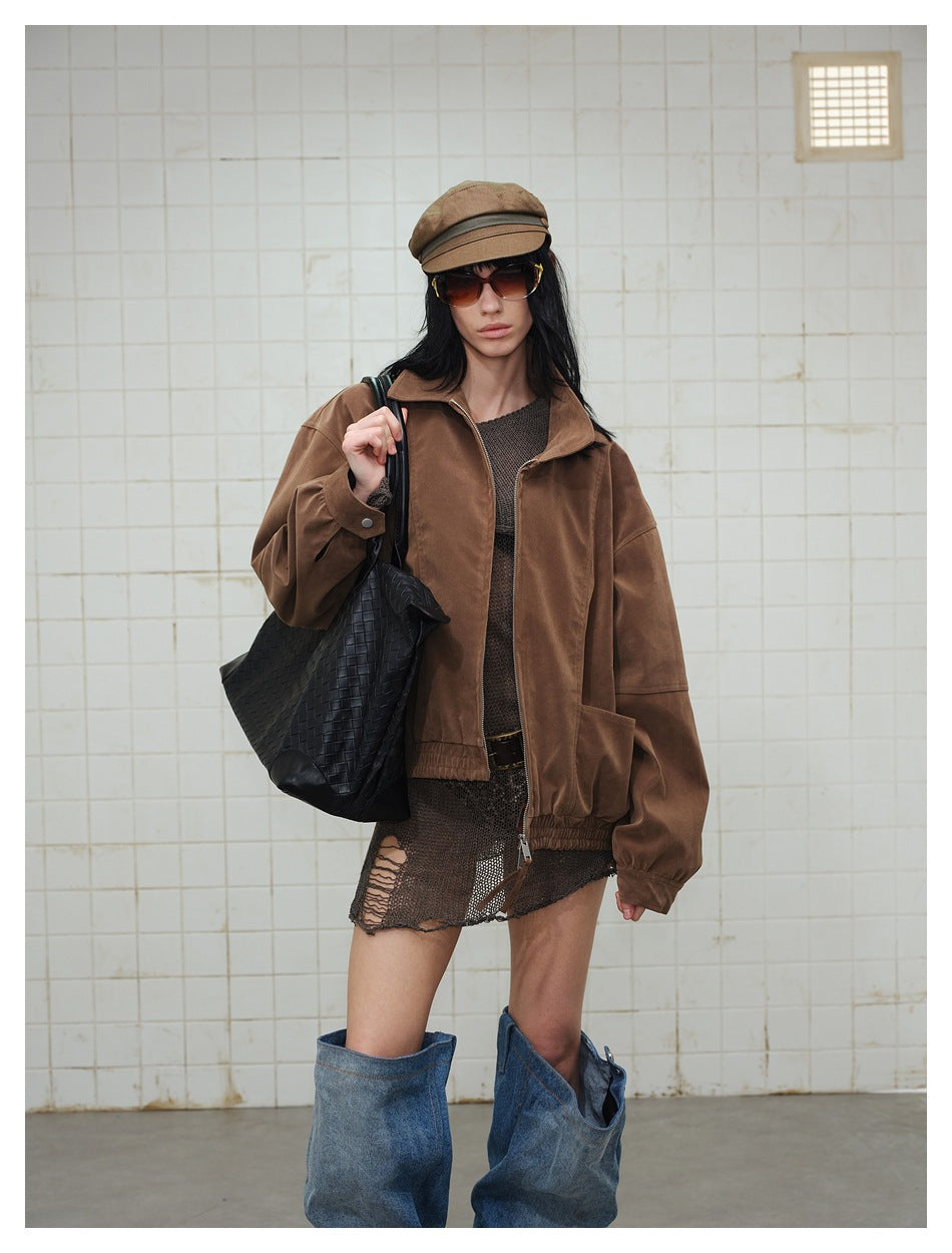 Model wearing an oversized brown zip-front jacket over a dark mesh mini dress, with slouchy blue denim boots.