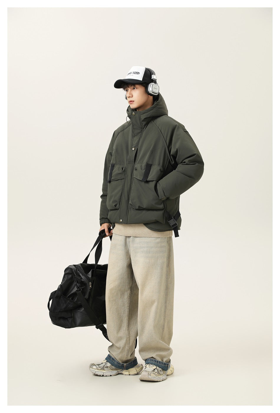 Model in a dark olive hooded jacket with large flap pockets, shown at an angle with a black duffel bag.