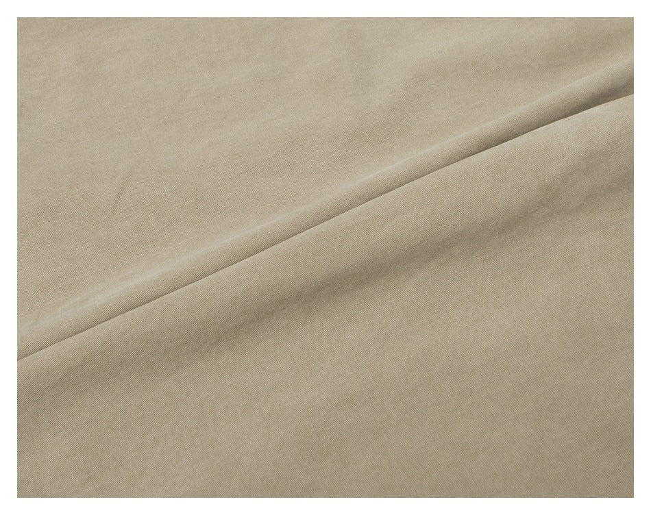 Extreme close-up of tan trouser fabric showing its fine diagonal weave and a fold.