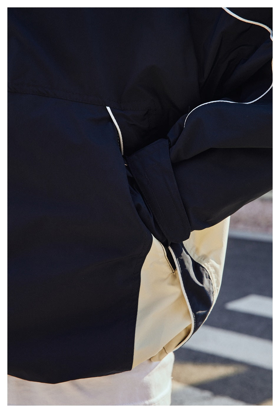 Close-up of the navy jacket's side pocket, sleeve cuff, white piping, and contrasting light side panel.