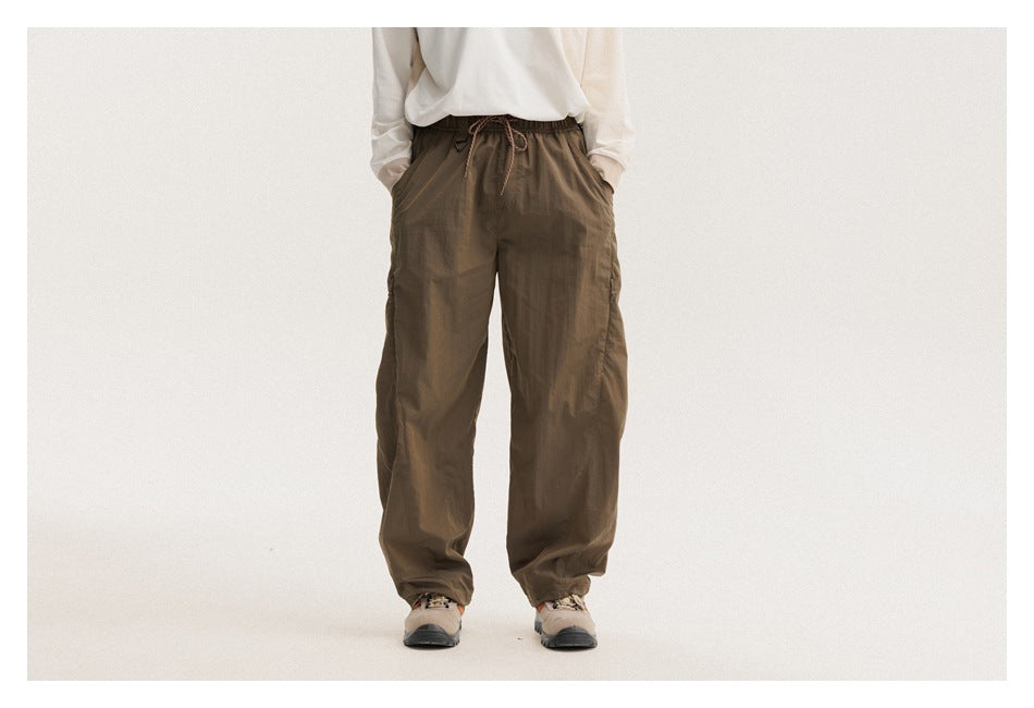Front view of a model wearing loose olive-brown drawstring pants with pockets and gathered ankle cuffs.