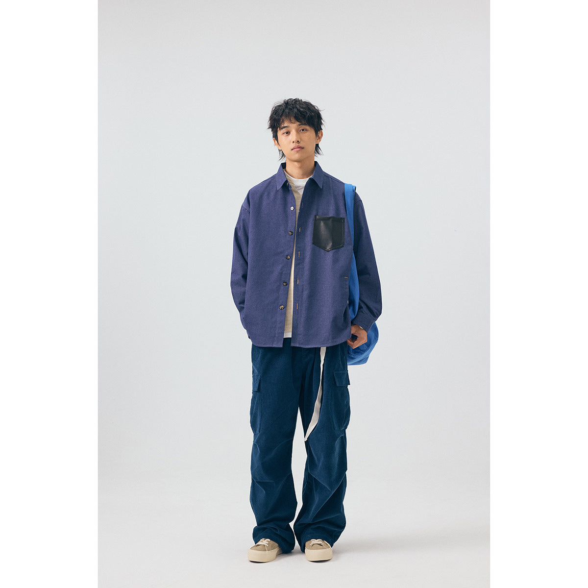 Full-length view of a model wearing a blue button-up shirt, cream top, dark cargo pants, and sneakers.