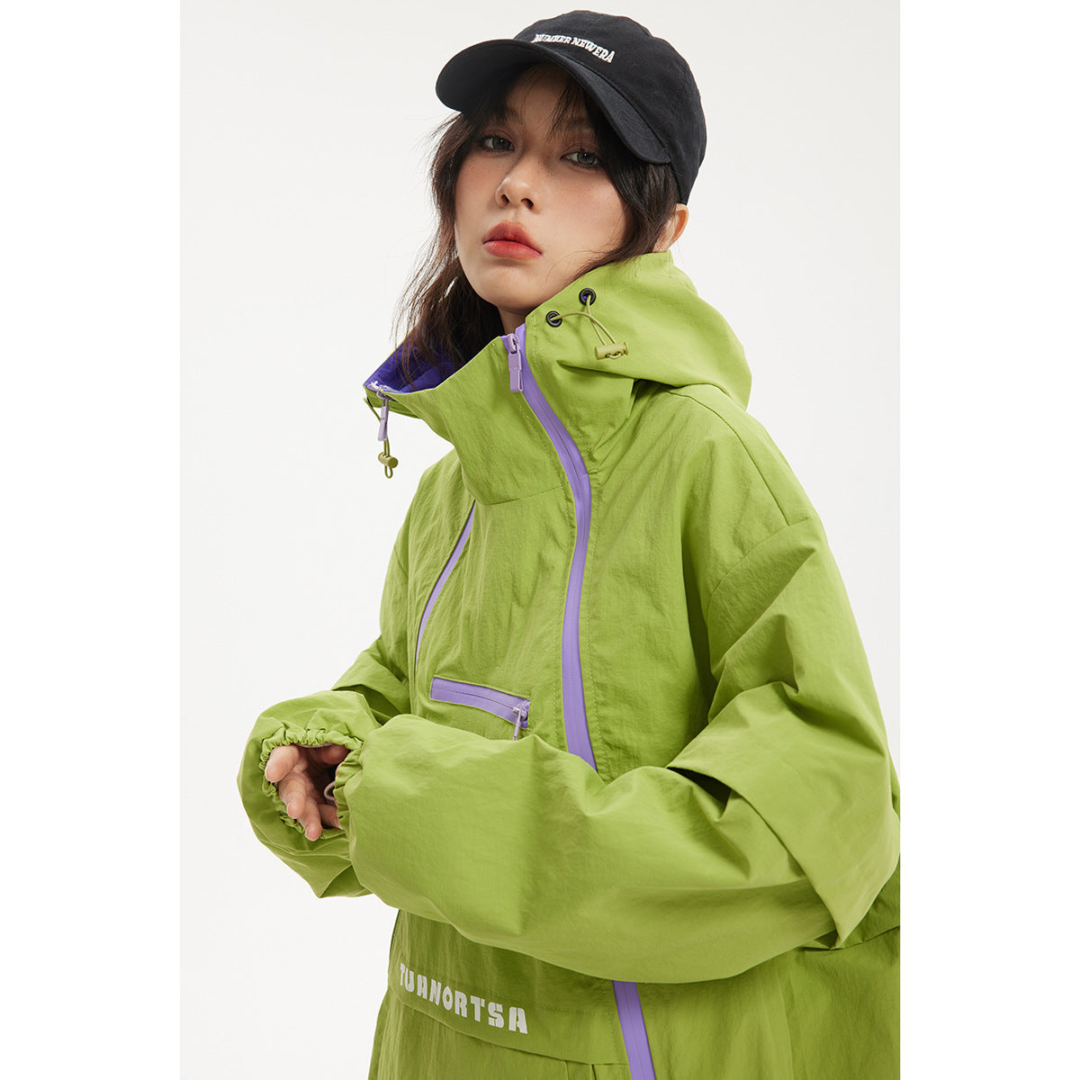 Close view of a model wearing a lime green jacket with a high hood, lavender zippers, and a small chest pocket.