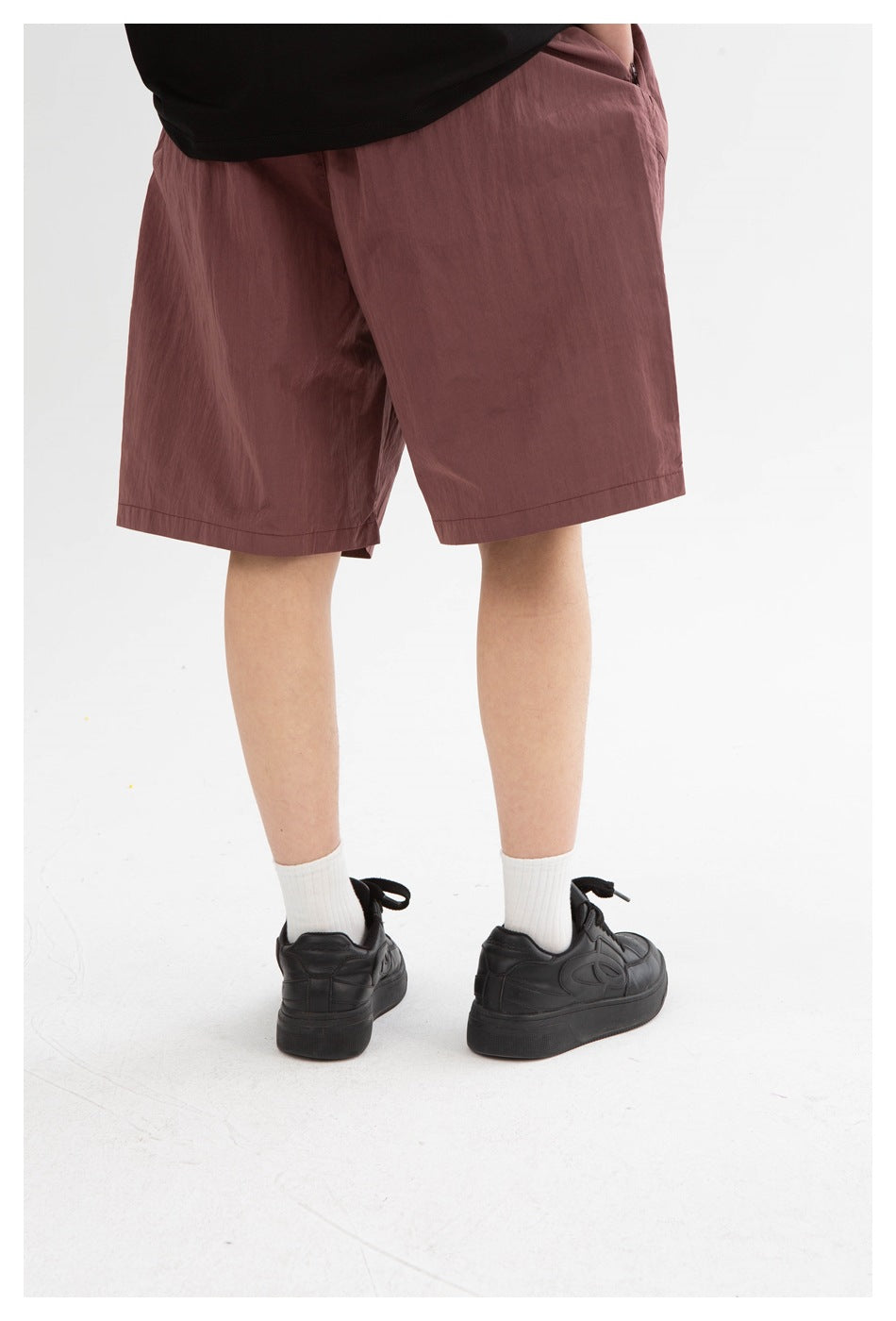 Close rear three-quarter view of a model wearing mauve knee-length shorts and black sneakers.