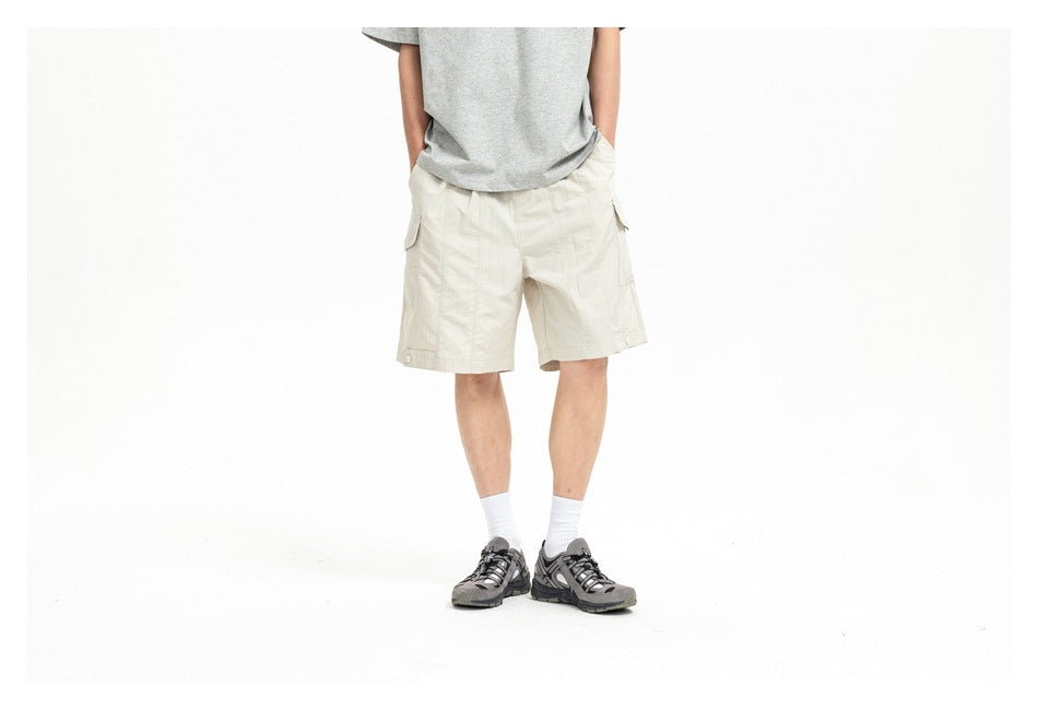 Person wearing beige cargo shorts with a gray t-shirt, white socks and gray sneakers, shown from the chest down
