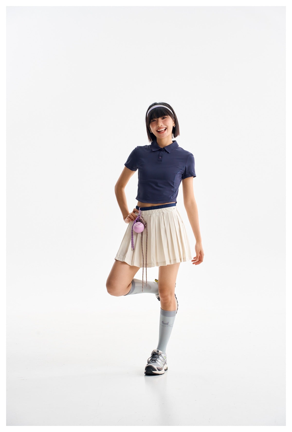 Model wearing a navy cropped short-sleeve polo with an ivory pleated skirt, knee-high socks and sneakers.