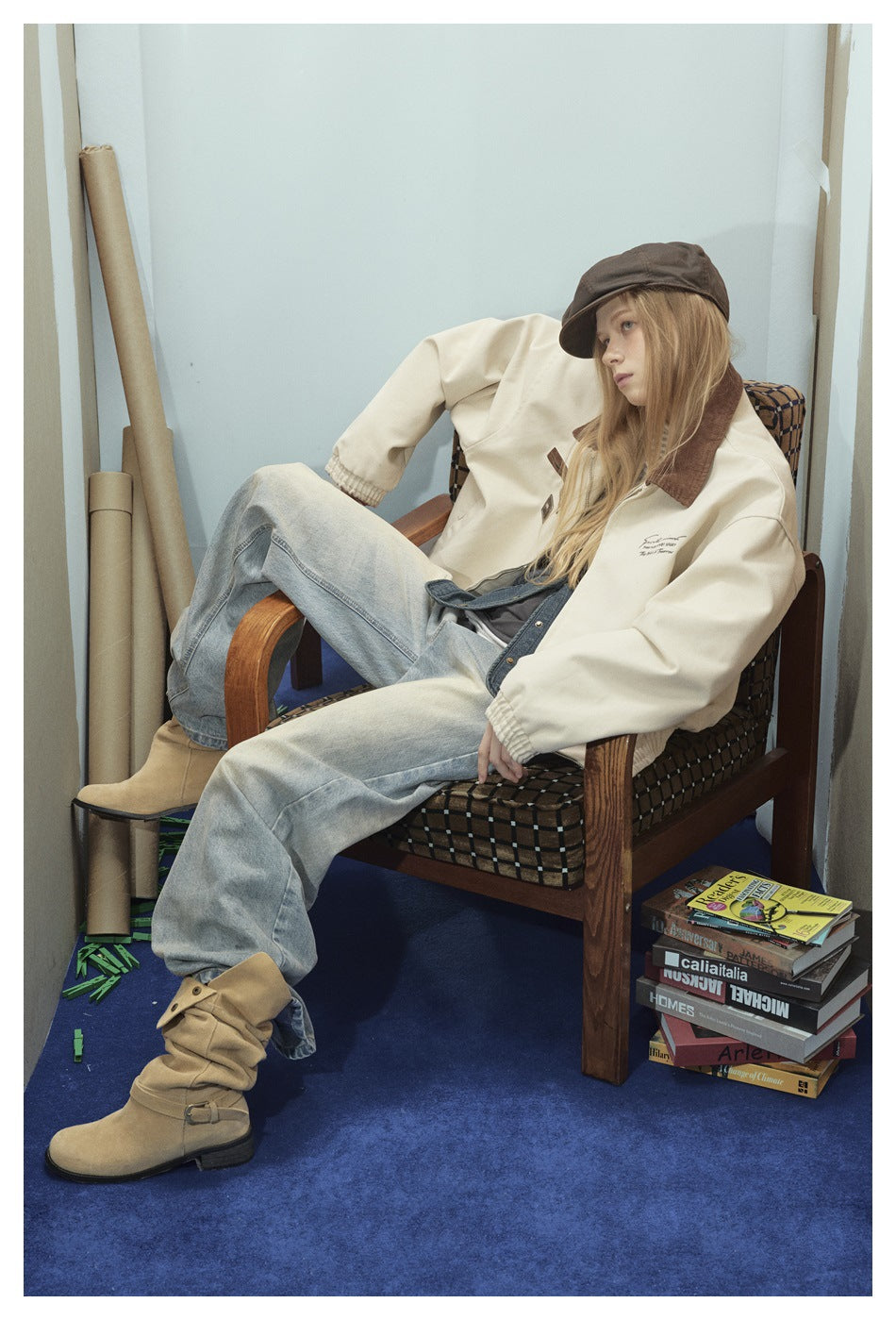 Model seated in a cream zip jacket with a brown collar, loose light-wash jeans and tan boots.