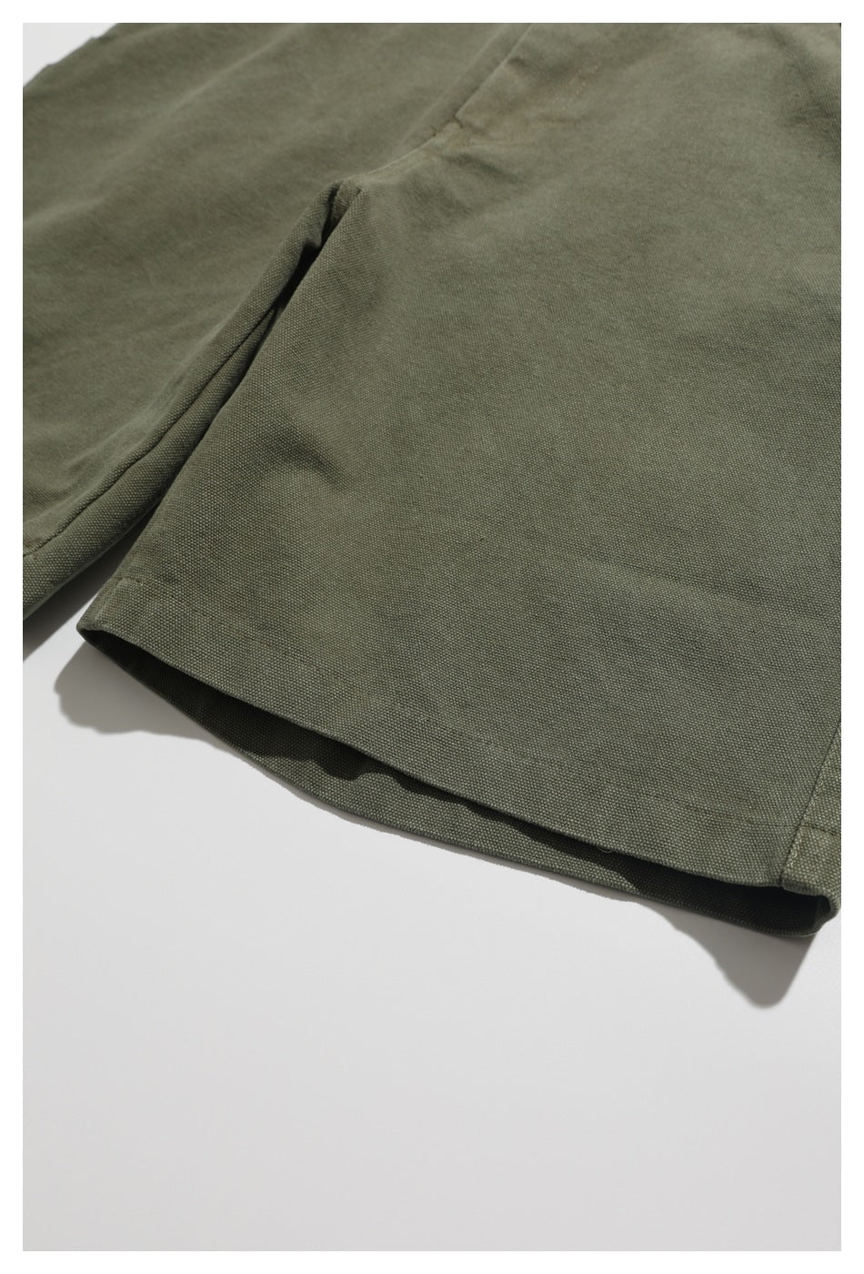 Close-up of the hem and stitching on olive-green shorts laid flat.