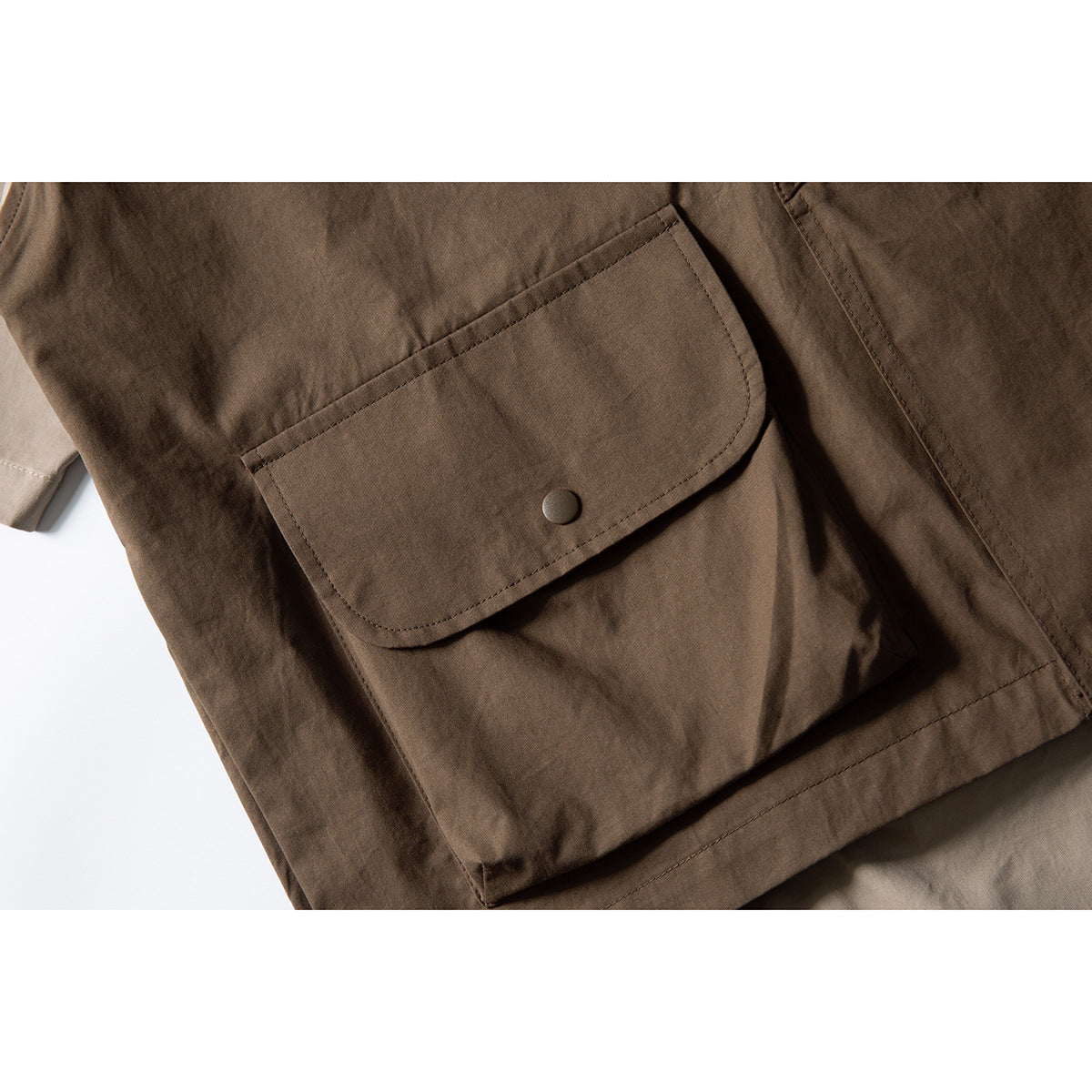 Close-up of a large flap pocket with a snap button on a brown utility vest.