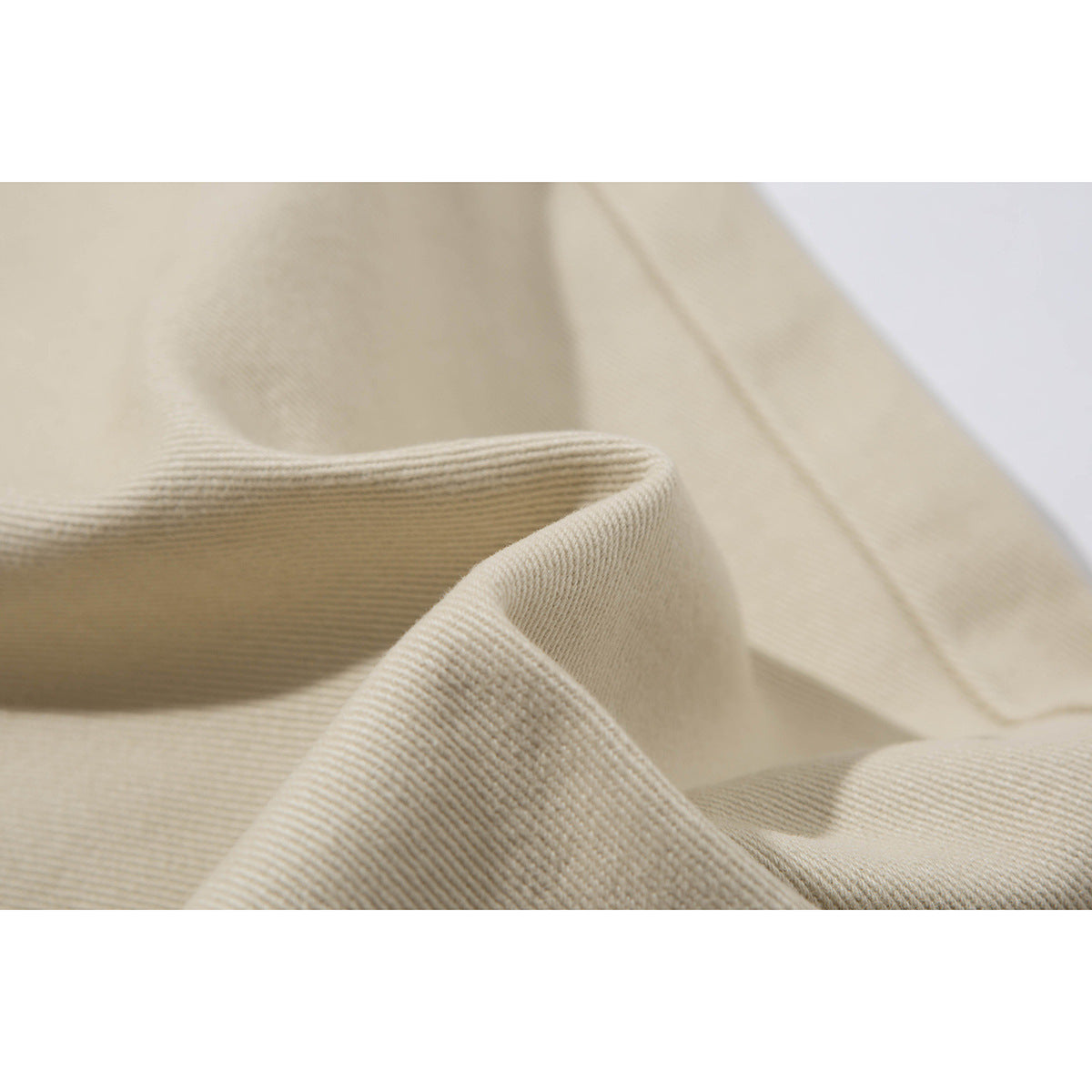 Close-up of beige trouser fabric folded to show its diagonal weave and texture.