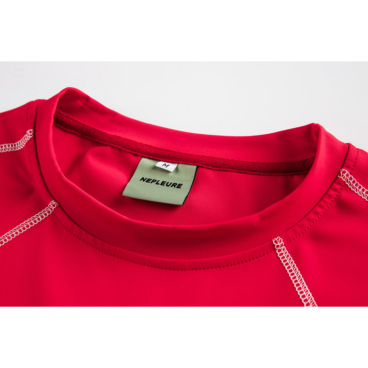 Close-up of a bright red shirt’s crew neckline, white contrast stitching and sewn-in NEPLEURE size M label.