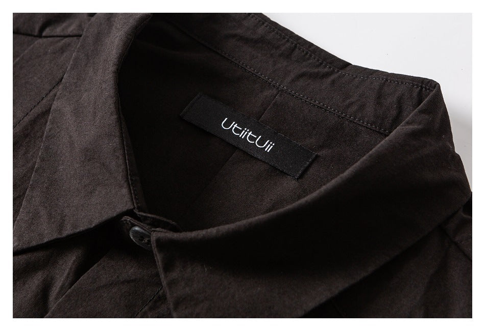 Close-up of a dark garment's pointed collar, button, and sewn-in neck label.