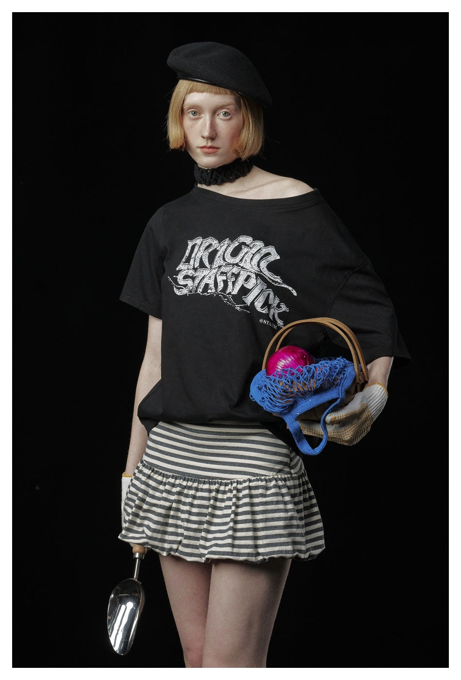 Close view of a black T-shirt with a large white stylized chest graphic, worn with a striped ruffle skirt.
