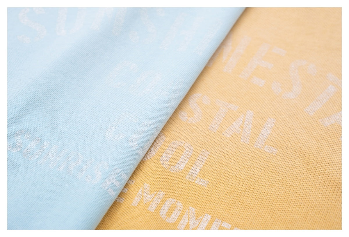 Close-up of light blue and golden-yellow fabric with pale printed lettering and a fine knit texture.