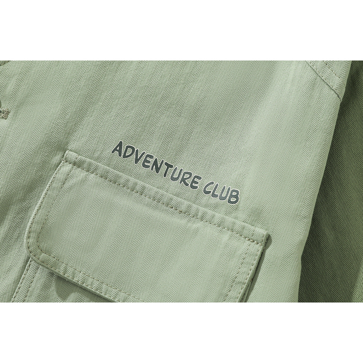 Close-up of a sage-green jacket chest pocket with white-outlined Adventure Club lettering.
