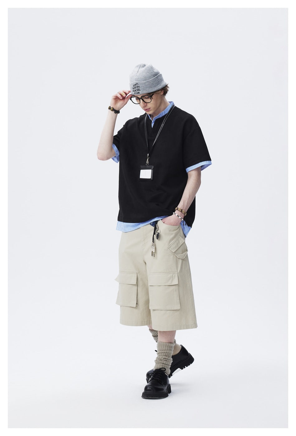Man in black layered striped-trim tee and beige cargo shorts, head tilted down with hand on beanie